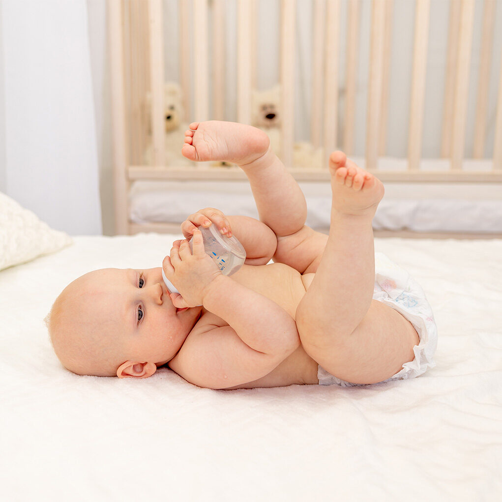 baby-boy-8-months-old-lying-diapers-white-bed-with-bottle-milk-home-feet-up-baby-food-concept-baby-drinking-water-from-bottle