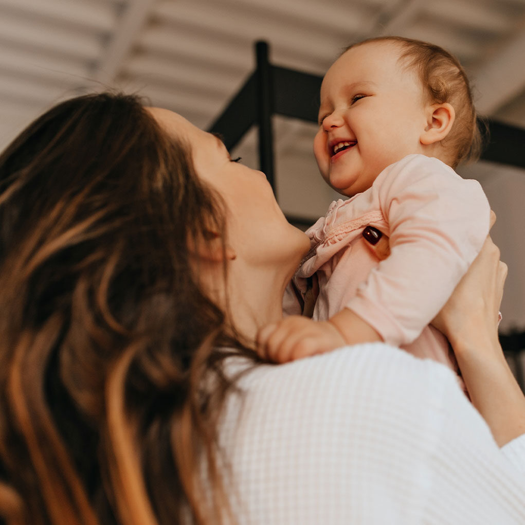 woman-with-long-hair-tickles-throws-up-laughing-baby-light-colored-home-sweater